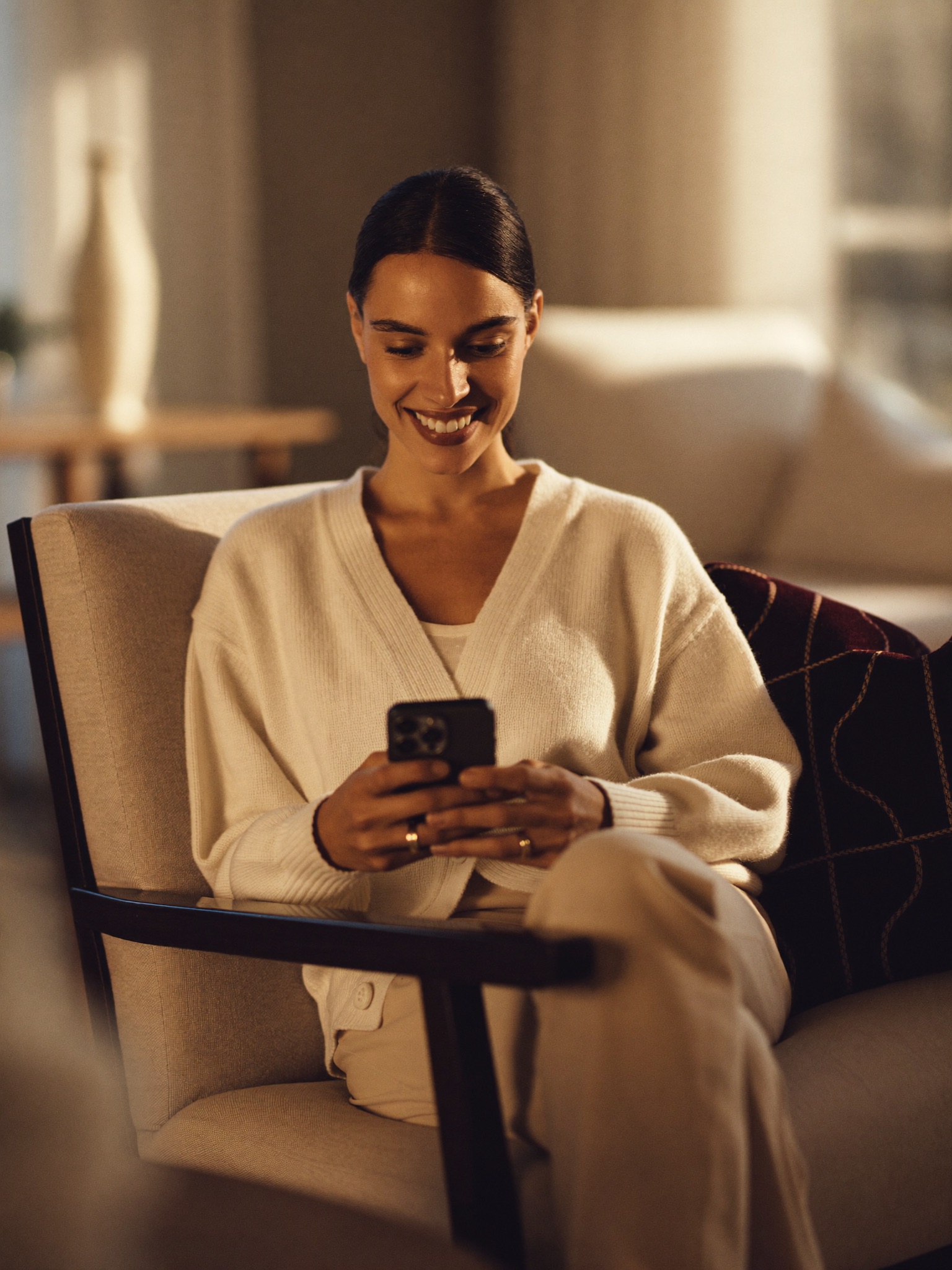 A mother relieved and at ease at home, checking her phone in warm natural light